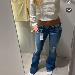 Blå bootcut jeans från Gina Tricot - Säljer ett par blå bootcut jeans från Gina Tricot i storlek S. Jeansen har låg midja, slitna detaljer på låren och klassisk femficksmodell. Perfekta för dig som gillar en avslappnad och trendig look.