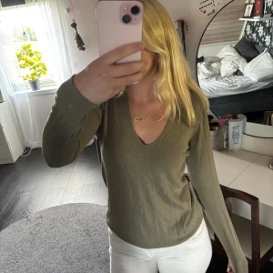 Olivgrön v-ringad tröja - Snygg olivgrön tröja med v-ringning och långa ärmar. Tröjan har ribbade muddar vid ärmslut och är tillverkad i ett mjukt, tunt material som passar perfekt till jeans eller kjol. Enkel och stilren design som är lätt att matcha.