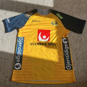 Gul och marinblå handbollströja från Craft  storlek M - Svensk landslagströja från Craft i storlek M. Tröjan är gul med marinblå ärmar, har tryckta sponsorer och SOFH-emblem på bröstet. Tillverkad i lätt och ventilerande funktionsmaterial, perfekt för träning eller match. Pris kan diskuteras 