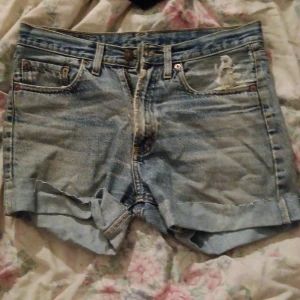 John Pearson & Son ljusblå jeansshorts - Säljer ett par ljusblå jeansshorts från John Pearson & Son med klassisk femficksdesign, uppvikta ben och knapp- samt dragkedja framtill. Shortsen har en snygg vintage-vibe och är perfekta för varma dagar. Märkespatch baktill och slitna detaljer för extra stil.