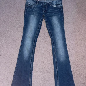 Low waisted mörkblå bootcut jeans från Amethyst - Snygga blå bootcut jeans från Amethyst med slitningar och ljusare partier framtill. Jeansen har klassiska fem fickor, dekorativa sömmar och detaljerade bakfickor. Materialet är 95% bomull, 4% polyester och 1% spandex för en skön stretch.Mått: midja tvärs över: 40cm Midje höjd: 17cm Innerbenslängd: 81cm Benvidd nertill: 20cm  skriv om ni vill ha bilder på hur den sitter!!