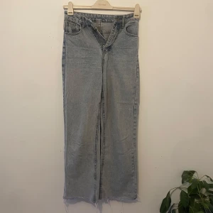 Ljusblå raka jeans med råa kanter - Säljer ett par ljusblå jeans med raka ben och råa, fransiga benslut. Klassisk femficksmodell med dragkedja och knapp. Jeansen har en avslappnad passform och är perfekta för en chill vardagslook.