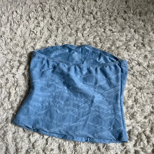 Blå bandeau tubtopp - Säljer en ljusblå bandeau tubtopp med diskret strukturmönster. Toppen är ärmlös och har en enkel, stilren design som passar perfekt till sommaren. Materialet känns mjukt och stretchigt för en bekväm passform.