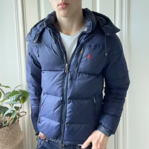 Polo Ralph Lauren dunjacka M - Polo Ralph Lauren dunjacka i storlek M, modellen är 180 fm 75 kg. Väldigt fin jacka där man kan spänna åt i midjan och många fina fickor med dragkedja. Minimal defekt där en tråd har typ dragits. Inget man märker av direkt. Asså det är väldigt litet håll. Kom med frågor! Äkta såklart 