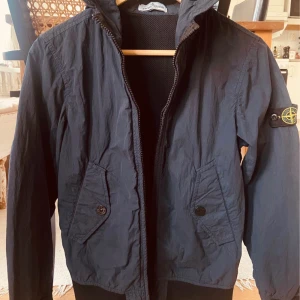 Mörkblå jacka från Stone Island strl 152.  - Junior, stl 12/ stl 152. 12 år.  Stone Island Jacka - Marinblå med luva och med två fickor framtill. Vår och höst. Knappt använd, i nyskick.  Hämtas på Östermalm eller post. 