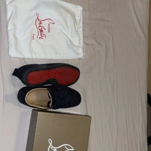 Christian Louboutin mörkblå mocka sneakers - Säljer ett par snygga mörkblå sneakers från Christian Louboutin i mjuk mocka med klassisk röd sula och broderad logga på hälen. Skorna har rund tå, platt sula och snörning. Innersulan är beige och ger en lyxig känsla. Box och dustbag medföljer pris kan diskuteras.