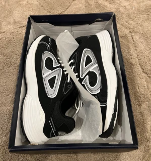  sneakers med vit sula - Säljer ett par svarta sneakers med vit och silverfärgad detalj på sidan och vit sula. Skorna har snörning och en sportig, chunky design Materialmix av textil och syntet ger en modern vibe. Perfekta för dig som vill sticka ut med lyxig streetstyle.