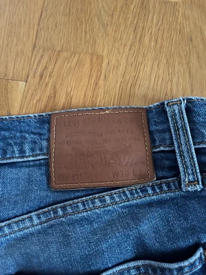 Levi's 511 blå jeans W30 L32 - Snygga Levi's Premium 511 jeans i klassisk blå tvätt med raka ben och fem fickor. Jeansen har normal passform och är tillverkade i slitstarkt denim med detaljer som knappgylf och bruna sömmar. Perfekt för dig som gillar tidlös stil och kvalitetsjeans.