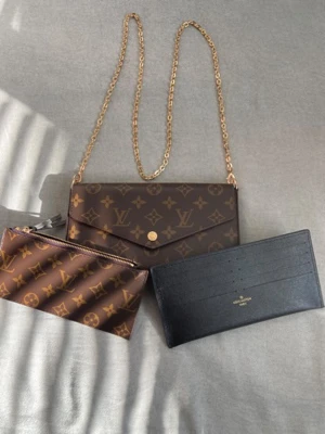 Louis Vuitton Monogram axelväska - Snygg axelväska från Louis Vuitton med klassiskt monogrammönster i brunt och beige. Väskan har guldfärgad kedja, kuvertformad design och medföljande plånbok och zip-pouch. Tillverkad i skinn med ikoniska LV-detaljer, perfekt för dig som gillar lyxiga accessoarer.