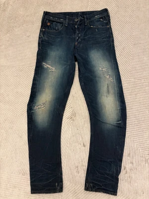 G star raw mörkblå jeans med slitningar - Snygga mörkblåa jeans från g star med slitna detaljer och mild washed detaljer. fint skick då bara använd ett fåtal gånger- storlek 29-30 midja och 32 långd, hör gärna av dig vid frågor! Pris går att diskutera vid snabb affär 👍