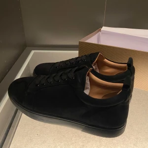 Svarta sneakers från Christian Louboutin - Snygga svarta sneakers från Christian Louboutin i mocka med klassisk röd sula och logga på insidan. Skorna har svarta snören och en stilren design som passar till allt. Insidan är i beige skinn för extra komfort. Har använts ett fåtal gånger, smutsen går säkert bort om du försöker tvätta bort det. Kom gärna med prisförslag😁