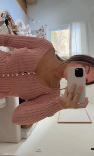 Rosa ribbad topp med pärlor från  NA-KD - Superfin rosa ribbad topp från NA-KD med v-ringning och pärlknappar längs hela framsidan. Klänningen har långärmade ärmar och sitter tight med snygg passform. Materialet är mjukt och stretchigt, perfekt för dig som gillar en feminin look.