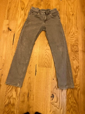 Grå raka jeansbyxor från HM - Säljer ett par grå jeansbyxor med klassisk femficksdesign och raka ben. Jeansen har normal passform och är tillverkade i mjukt denimtyg. Färgen är en snygg, lite urtvättad grå ton som passar till det mesta. Perfekt för dig som gillar enkel och stilren look.