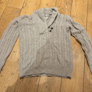 Massimo Dutti Kashmir kabelstickad kofta - En snygg Kashmir kabelstickad kofta från Massimo Dutti i angora och kashmirmix. Koftan har en bred krage med två bruna knappar framtill och ribbade muddar. Perfekt för kallare väder. Tveka inte på att komma med frågor, pris ej huggit i sten. 