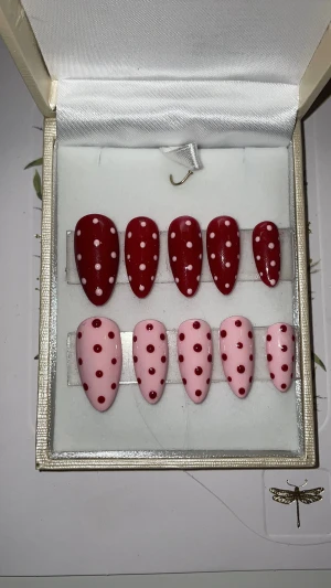 Rosa och röda prickiga lösnaglar - Säljer ett set med 10 st handgjorda lösnaglar i almondform, hälften i mörkrött med ljusrosa prickar och hälften i ljusrosa med mörkröda prickar. Perfekt för dig som vill ha en söt och lekfull look. STORLEK: S, skriv om annan storlek behövs😊