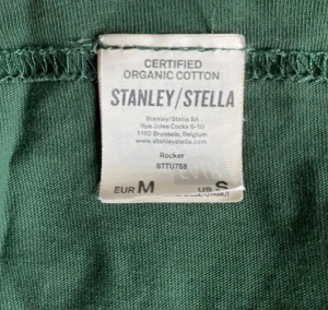 Olivgrön NOCCO x 7-Eleven t-shirt -storlek Medium  - Säljer en grön t-shirt från Stanley/Stella i ekologisk bomull med tryck i gult och vitt: 'I'M POWERED BY NOCCO' och loggor för NOCCO och 7-Eleven. Klassisk rund hals och korta ärmar, perfekt för dig som gillar energidrycksvibbar.