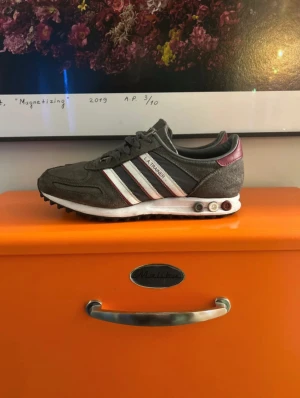 Adidas LA Trainer grå sneakers - Säljer ett par Adidas LA Trainer sneakers i mörkgrå, skorna är i bra skick det finns en defekt kolla sista bilden. Skriv om ni undrar över något! 