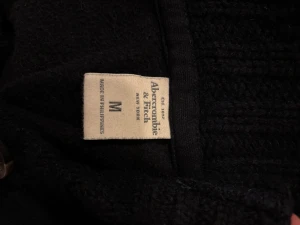 Mörkblå kofta Abercrombie & Fitch - Snygg mörkblå kofta från Abercrombie & Fitch med ribbad krage och knappar hela vägen framtill. Den är liten i storleken så passar även S. Tröjan har ett broderat vitt älg-logo på bröstet, två fickor och är tillverkad i mjuk bomull med stickade detaljer vid kragen och knappslån. Perfekt för chill höstkvällar.