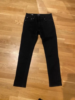 Svarta slim jeans från Jack & Jones - Svarta jeans från Jack & Jones, modell Slim/Glenn. Snygg, smal passform med klassisk femficksdesign och knappstängning. Jeansen är tillverkade i stretchigt denim för extra komfort och har en stilren look som funkar till många olika outfits.