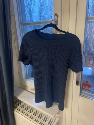 Svart ribbad topp med kort ärm - Säljer en svart topp med ribbad struktur och rund hals. Toppen har korta ärmar och är tillverkad i ett mjukt, stretchigt material som ger en skön passform. Perfekt för dig som gillar enkel och stilren design med lite extra textur.