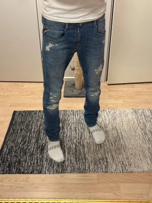 Replay Anbass blå jeans med slitningar - Säljer ett par Replay Anbass jeans i blå tvätt med coola slitningar och detaljer på benen. Köpta för ett år sedan men knappast använda. Nytt skick. Pris kan diskuteras vid snabb affär.