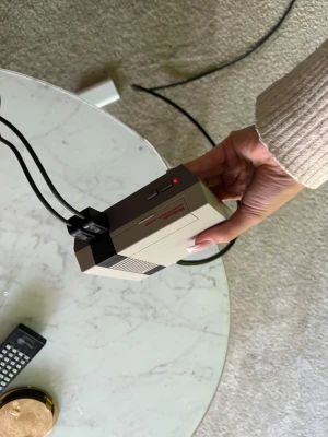 Nintendo Entertainment System Classic Mini - Nintendo Classic Mini NES med originalkontroll. Konsolen är i fint skick, inga synliga repor eller skador. Perfekt för retrospel och samlare. Fungerar utmärkt, strömindikatorn lyser och kontrollen är ren och hel. Det finns 2 kontroller till.