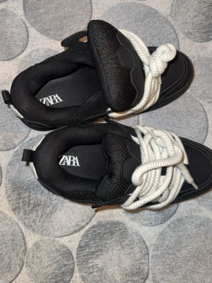 Svarta chunky sneakers från Zara - Säljer ett par svarta chunky sneakers från Zara med grova vita snören. Skorna har en modern och sportig look med meshdetaljer och tjock sula. Perfekta för dig som gillar statement-sneakers och vill sticka ut lite extra.