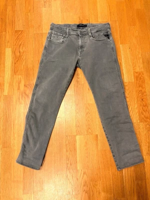 Replay Anbass  - Snygga grå slim fit jeans från Replay med klassisk femficksdesign och diskreta sömmar på bakfickorna. Jeansen har dragkedjegylf och är tillverkade i stretchigt denimtyg för en bekväm passform. Perfekta för en stilren och avslappnad look.