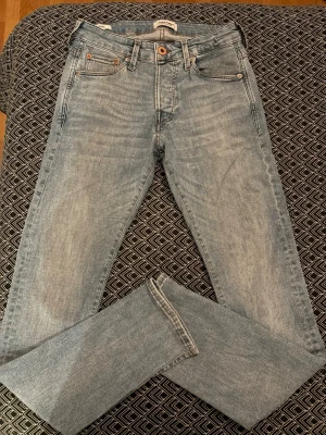 Ljusblå raka jeans från Jack & Jones  - Snygga ljusblå jeans från Jack & Jones med klassisk femficksdesign och raka ben. Jeansen har en ljus tvätt och subtila slitningar för en avslappnad look. Tillverkade i mjukt bomullstyg som ger en skön känsla hela dagen. Hål vid vänstra baksidan men inget man ser mycket när du har på dig dem.