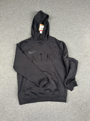 Svart AIK hoodie från Nike - Snygg svart hoodie från Nike med AIK-tryck på bröstet och AIK-logga på ärmen. Klassisk känguruficka framtill och huva med dragsko. Perfekt för dig som vill representera AIK med stil. Tillverkad i mjukt material för maximal komfort.