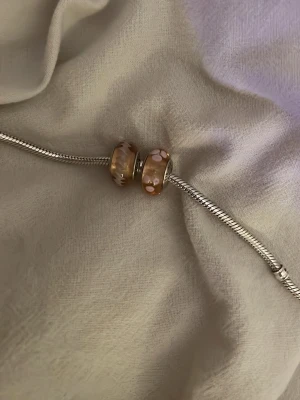 Pandora berlocker glaspärlor - Fina rosa berlocker från Pandora, en med blommor och en med ”ränder” passande om du vill fylla ditt berlock armband💕