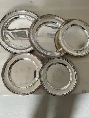 Gamla antika Fem silverfärgade metallfat - Gamla. Antika Säljer ett set med fem runda fat i silverfärgad metall. Faten har en klassisk, enkel design med upphöjd kant och varierar något i storlek. Perfekta som dekoration eller serveringsfat. Snygga att ha framme på bordet.