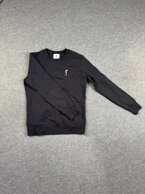 Svart sweatshirt från RS Sports - Stilren svart sweatshirt från RS Sports med rund halsringning och diskret vitt logotryck på bröstet. Perfekt för en clean och avslappnad look.