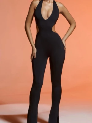 Svart halterneck jumpsuit med cut-outs - Säljer en svart, tight jumpsuit med halterneck och snygga cut-outs i midjan. Modellen har utsvängda ben och öppen rygg med knäppning i nacken. Perfekt för dig som vill sticka ut och köra en trendig look.