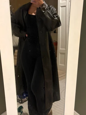 Svart lång trenchcoat i skinnimitation - Snygg brun trenchcoat i skinnimitation. Köpt från Mango. Använd endast 1 gång. Lång lite mer rak modell. 