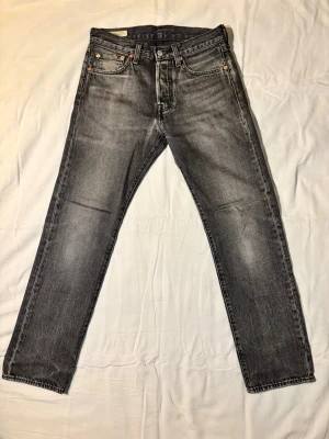 Grå Levi's 501 raka jeans - Snygga grå 501 jeans från Levi's med raka ben och klassisk femficksdesign. Jeansen har en cool tvättad look och detaljer som nitar och läderpatch bak i midjan. Perfekta för dig som gillar en avslappnad och tidlös stil.