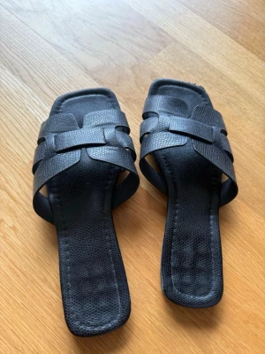 Svarta flätade sandaler med fyrkantig tå - Stilrena svarta sandaler med breda flätade remmar och fyrkantig tå. Tillverkade i ett strukturerat konstläder som ger en trendig look. Perfekta för dig som gillar minimalistisk och modern stil.