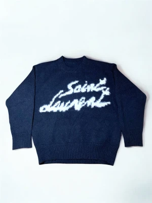 Svart Saint Laurent stickad tröja - Stickad svart tröja från Saint Laurent med vit, fluffig logotyp framtill i grafisk stil. Tröjan har rund halsringning, långa ärmar och ribbstickade muddar. Perfekt för dig som gillar statement-plagg och exklusiva märken.