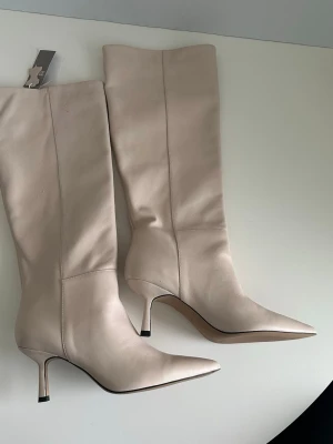 Beige knähöga stövlar i äkta läder - Helt NYA eleganta beige / cremefärgade / vita knähöga stövlar i äkta läder från H&M i storlek 40. Klassisk spetsig tå och smal klack. Perfekt för både vardag och fest. Helt nya men har små rivsår från ivrig katt på skaftet, se bilder, inget som syns eller som man tänker på när man har dem på dock. Nypris 2200:-.  Hämtas i Stockholm eller skickas mot porto. 