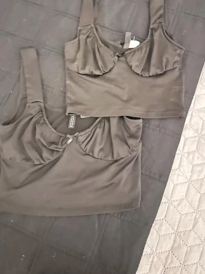 Svarta bodys från Nelly, 2-pack - Två svarta bodys från Nelly med breda axelband och lätt rynkade kupor. Mjukt och stretchigt material som sitter skönt mot kroppen. Perfekta att styla under skjorta eller kavaj. Säljes som set.