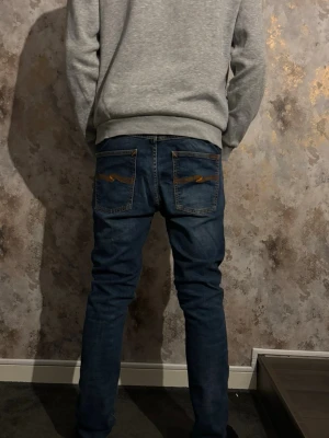 Mörkblåa nudie jeans - Snygga mörkblå slim fit jeans med tydliga kontrastsömmar och stora bakfickor med dekorativa detaljer. Pris går att diskutera