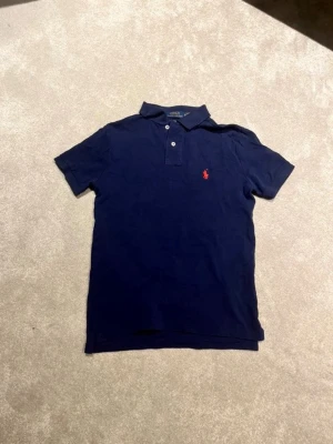 Ralph Lauren Piké - Klassisk mörkblå pikétröja från Ralph Lauren med korta ärmar och krage. Den är i storlek XS och är ett perfekt plagg inför kommande säsong! Säljs pga att den inte passar längre, är i mycket bra skick! Hör av er om minsta fundering💫
