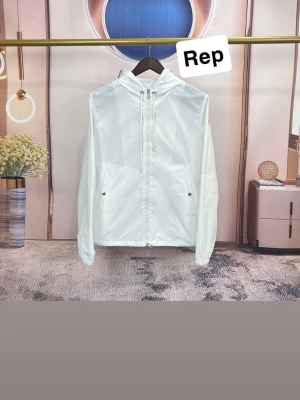 Moncler liknande jacka - Stilren vit vindjacka med huva och dragsko. Jackan har dragkedja framtill och två fickor med knappstängning. Perfekt för blåsiga dagar och enkel att matcha med olika outfits.