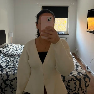 Vit kofta med v-ringning - Säljer en stilren vit kofta med djup v-ringning och lång ärm. Koftan har en loose passform och är tillverkad i ett mjukt stickat material som känns skönt mot huden. Perfekt att slänga på sig över en topp för en enkel och clean look.