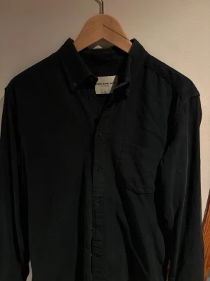 Mörkgrön manchesterskjorta med bröstficka - Stilren svart skjorta från These Glory Days i mjuk manchester. Skjortan har klassisk krage, knäppning framtill och en bröstficka. Perfekt för dig som gillar en enkel men snygg look.