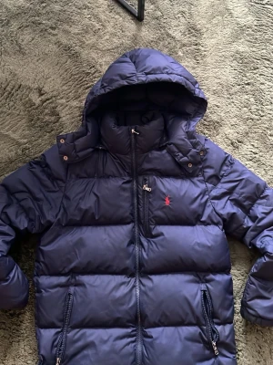 Mörkblå dunjacka från Polo Ralph Lauren - Tjena säljer min Polo Ralph Lauren jacka som är XL i junior storlek men passar S. Inga skador eller något annat på den bara dragkedjan på ena sidan som inte går att dra upp