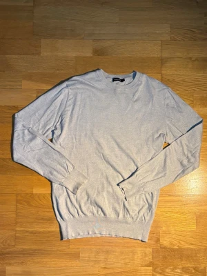 Ljusgrå stickad tröja från J.Lindeberg - Snygg ljusgrå stickad tröja från J.Lindeberg i storlek S. Tröjan har rund hals, ribbade muddar och är långärmad. Perfekt för dig som gillar stilrena och enkla plagg med en clean look. Materialet är mjukt och skönt mot huden.