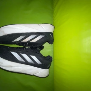 Svarta Adidas Löparskor - Säljer ett par svarta Adidas sneakers med klassiska vita ränder på sidan och tjock vit sula med Lightmotion-teknologi. Skorna har snörning och mesh-överdel för bra ventilation. Perfekta för dig som gillar sportig stil och vill ha bekväma skor till träning eller häng. Sulor ingår ej, så skorna kommer utan sula. Inga returer😉