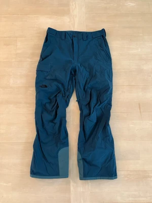 Blå skidbyxor från The North Face - Säljer ett par blå skidbyxor från The North Face. De är i fint skick utöver en reva på nedre delen av benet som enkelt går att laga med en täcklapp. Ny pris är ca 3000kr. 
