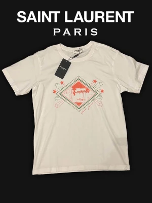 Vit Saint Laurent t-shirt med tryck - Säljer en vit t-shirt från Saint Laurent, storlek M och är mer av en slim fit så passar för dig som är smal, 66 cm i längd och 100cm i bröst. helt ny aldrig använd